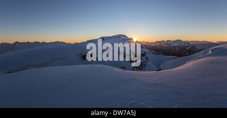 Sun at sunset on the peaks of Trentino Dolomites. Winter season. Latemar massif in background. Italian Alps. View from Col Margherita mountain. Stock Photo