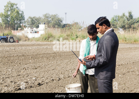 farmer working in plowedfield and busineeman standing with laptop Stock Photo