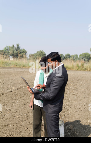 farmer working in plowedfield and busineeman standing with laptop Stock Photo