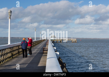 Two people, and elderly couple, standing on pier at Yarmouth, Isle of Wight, UK looking at view over Solent Stock Photo