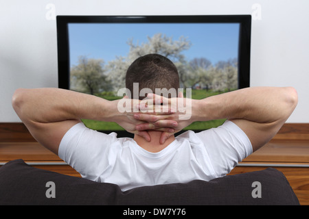 Young man sitting on a sofa and watching tv Stock Photo