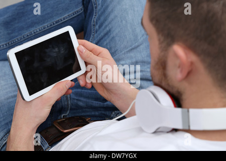A young man with headphones is listening to music on his tablet computer Stock Photo