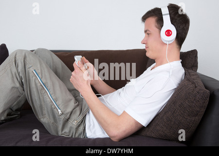 A young man with headphones is listening to music on a sofa Stock Photo