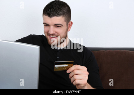A young man is sitting on a sofa and doing internet shopping Stock Photo