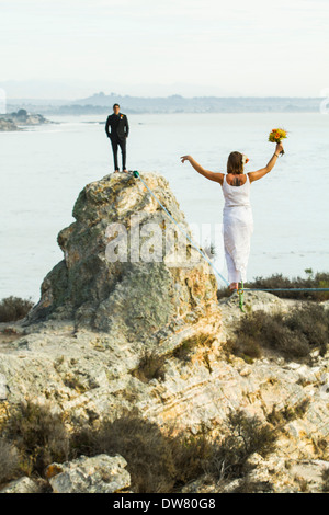 Woman walks a slack line high above ground to her soon to be husband waiting on the rock in the distance Stock Photo