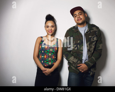 Portrait of beautiful young woman and handsome young man standing wearing casual hipster outfits. Couple posing against gray. Stock Photo