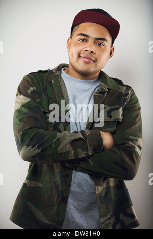 Handsome young man wearing camouflage jacket and cap with his arms crossed looking at camera with smile. Stylish young male. Stock Photo