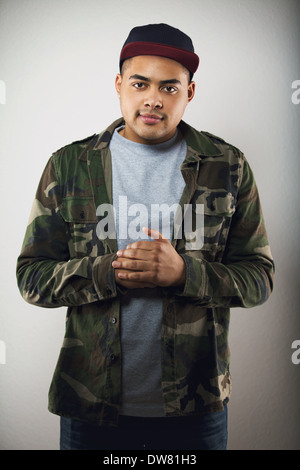 Handsome male fashion model posing in casual wear on grey background. Young man looking at camera wearing camouflage jacket. Stock Photo
