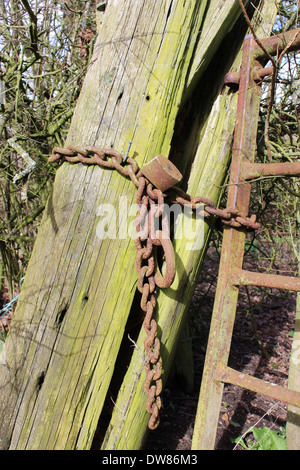 Rusty lock and chain on metal farm gate with leaning wooden post Stock Photo