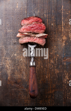 Slices of beef steak on meat fork on wooden background Stock Photo