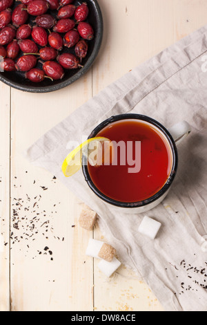 Top view on vintage white mug of tea with lemon and briar berries, served with sugar cubes over white wooden table Stock Photo