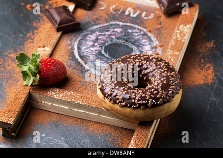 Chocolate and drawing donuts with fresh strawberries and dark chocolate served on chalkboard over black stone table. Stock Photo