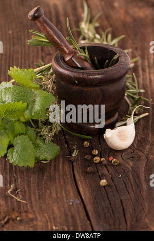 garlic, mint and rosemary in wooden vintage mortar on old wooden table Stock Photo