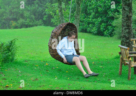 Eastern Highlands of Zimbabwe in summer with bright green colours and mountainous habitat. Man in hanging wicker swing chair Stock Photo