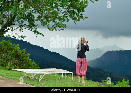 Eastern Highlands of Zimbabwe in summer with bright green colours and mountainous habitat. Woman with red trousers photographing Stock Photo