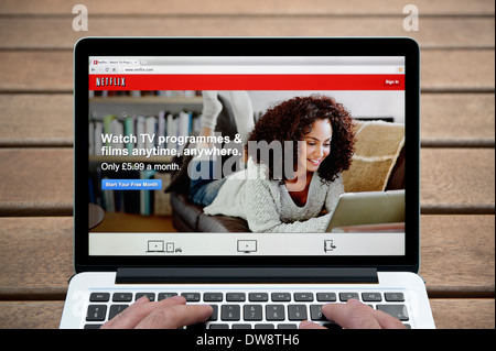 The Netflix website on a MacBook against a wooden bench outdoor background including a man's fingers (Editorial use only). Stock Photo