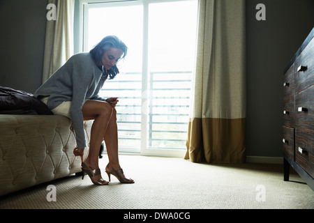 Mature woman sitting on bed putting on high heels Stock Photo