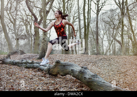 Young woman jumping over log in forest Stock Photo