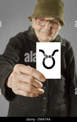 Elderly woman holding card with printed horoscope Taurus sign. Selective focus on card and fingers. Stock Photo