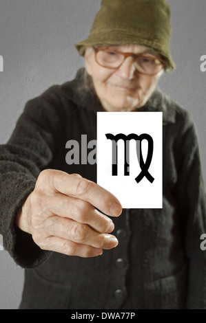 Elderly woman holding card with printed horoscope Virgo sign. Selective focus on card and fingers. Stock Photo