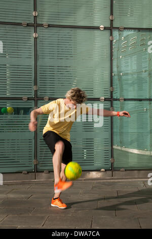 Manchester UK. European Freestyle Soccer Champion John Farnworth, MR, showing his football 'Keepy Uppy' skills, tricks, fun, lifestyle, fitness, happy, practice, recreation, talented , exercise, game, kicking football, a Pelé-inspired freestyle performance, in the streets near the Urbis National Football Museum.  World Cup 100 Day Countdown Carnival a day of celebrations as Mardi Gras to celebrate the beginning of the 100 day countdown to this year’s World Cup!  John is a football freestyler and entertainer who holds four Guinness World Records including the most around the worlds in a minute. Stock Photo