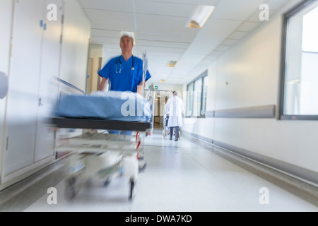 Stretcher or gurney & a wheelchair being pushed at speed through a hospital corridor by doctors & nurses to an emergency room Stock Photo