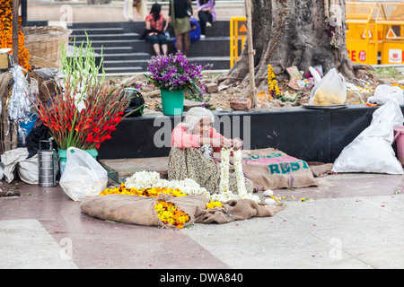 Old Indian woman at a flower stall sitting on the pavement making garlands to sell at a nearby Hindu temple, New Delhi, India Stock Photo