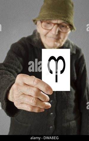 Elderly woman holding card with printed horoscope Aries sign. Selective focus on card and fingers. Stock Photo