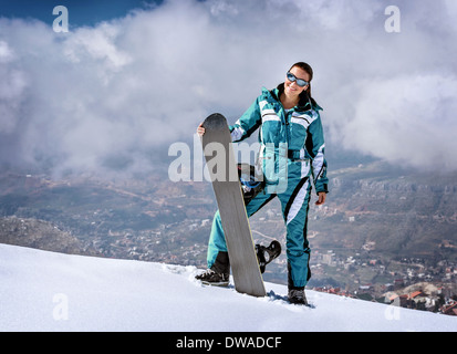 Sportive woman standing on the top of mountain with snowboard in hands, active wintertime holidays, extreme lifestyle concept Stock Photo
