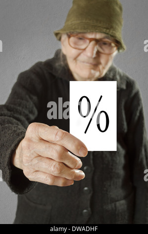 Elderly woman holding card with printed percent sign. Selective focus on card and fingers. Stock Photo