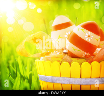 Easter eggs in the basket on fresh green grass, bright yellow sun light, eggs painted with red colours and floral ornament Stock Photo