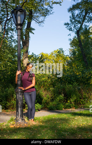 A smiling woman leaning against a lamp post in the park Stock Photo