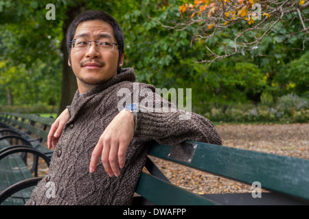 an Asian man in his twenties relaxing on a bench in a park Stock Photo