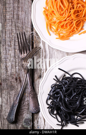 Top view on plates with black and orange spaghetti served with vintage forks on old wooden table Stock Photo