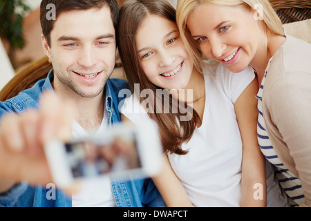 Young man holding cellular phone with happy daughter and wife near by Stock Photo