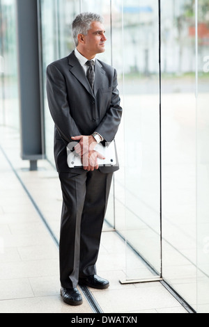 thoughtful senior businessman holding a laptop in modern office Stock Photo
