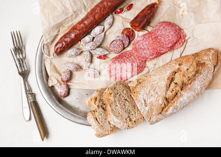 Set of salami served with fresh bread on old wooden cutting board. Stock Photo