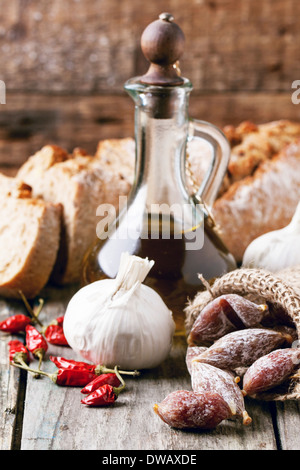 Little salami in a sack with red hot chili peppers, garlic, olive oil and fresh bread over old wooden table. Stock Photo