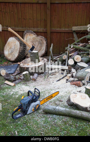 An axe in a piece of wood on a chopping block and a Ryobi chain saw for making firewood, England, UK Stock Photo