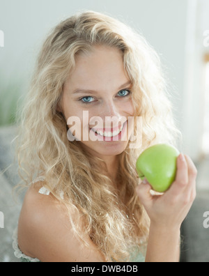 Portrait of happy young woman holding apple in house Stock Photo