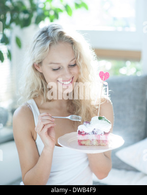 Beautiful woman having raspberry cake with fork in house