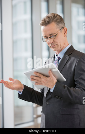 Businessman gesturing while using tablet PC in office Stock Photo