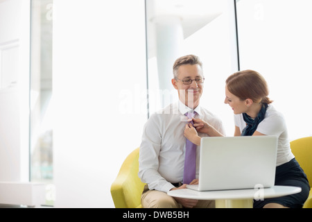 Businesswoman putting on tie to male colleague at lobby Stock Photo