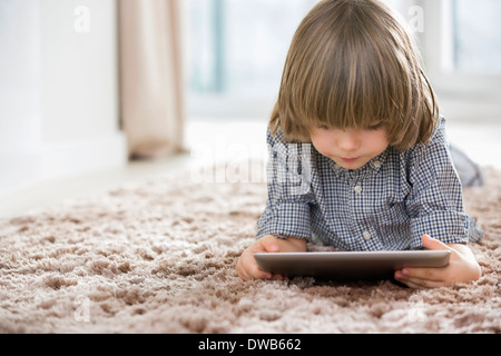 Boy using digital tablet while lying on rug at home Stock Photo