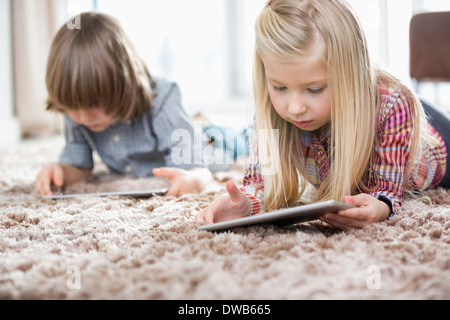 Cute girl and brother using digital tablets on rug in living room Stock Photo