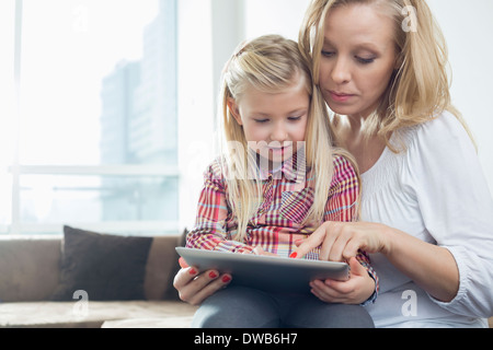 Happy woman with daughter using digital tablet in living room Stock Photo