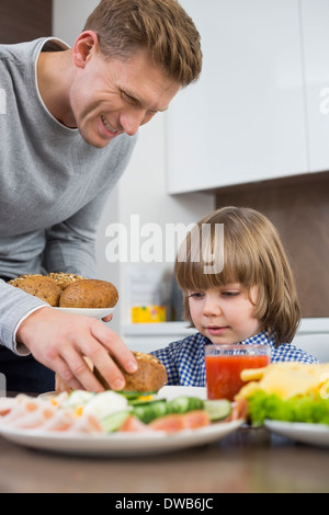 Happy father serving meal to son at table in kitchen Stock Photo