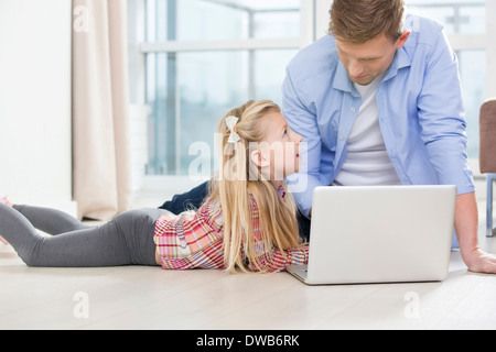 Father and daughter using laptop on floor in living room Stock Photo