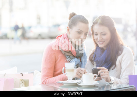 Happy women using cell phone at sidewalk cafe during winter Stock Photo