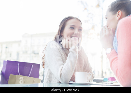 Beautiful young woman looking at friend sharing secrets at outdoor cafe Stock Photo